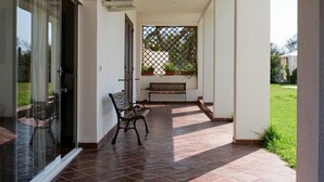 Un espace extérieur abrité, doté d’un sol carrelé, d’un banc et d’une porte vitrée donnant sur une terrasse.