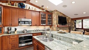 A modern kitchen with granite countertops, stainless steel appliances, wooden cabinets, and a stone accent wall.