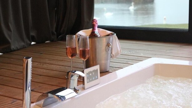 A spa area with a bathtub, a champagne bottle, and two glasses of wine on a wooden deck. - Serenity Resort (Codlea)