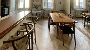 A dining room with a long wooden table, several chairs, a chandelier, and large windows with curtains. - Charming Artistic and Historic Chartrons Flat with Private Patio
 (Bordeaux)