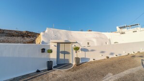 Un bâtiment blanc avec une porte et deux plantes en pot, un chemin de gravier et un ciel bleu dégagé.