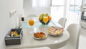 Une cuisine moderne avec des meubles blancs, une table à manger avec des chaises, un panier de fruits et un verre de jus d’orange.