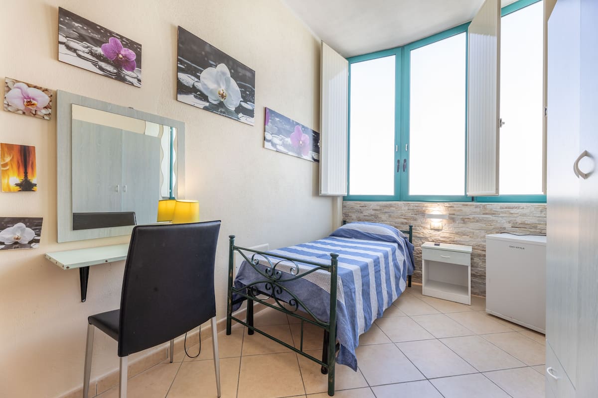 Un dormitorio con cama, un escritorio con silla, armario y ventana con cortinas.
