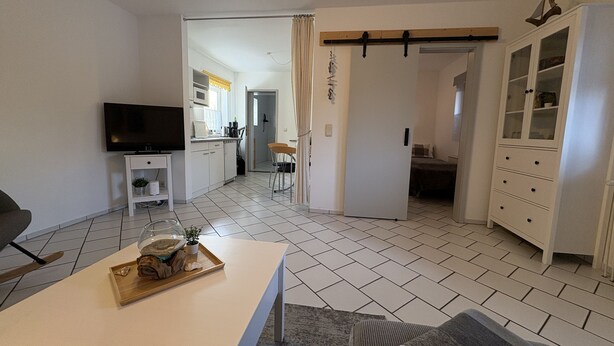 Un soggiorno moderno con una televisione a schermo piatto, un'area pranzo con tavolo in legno e una cucina sullo sfondo.