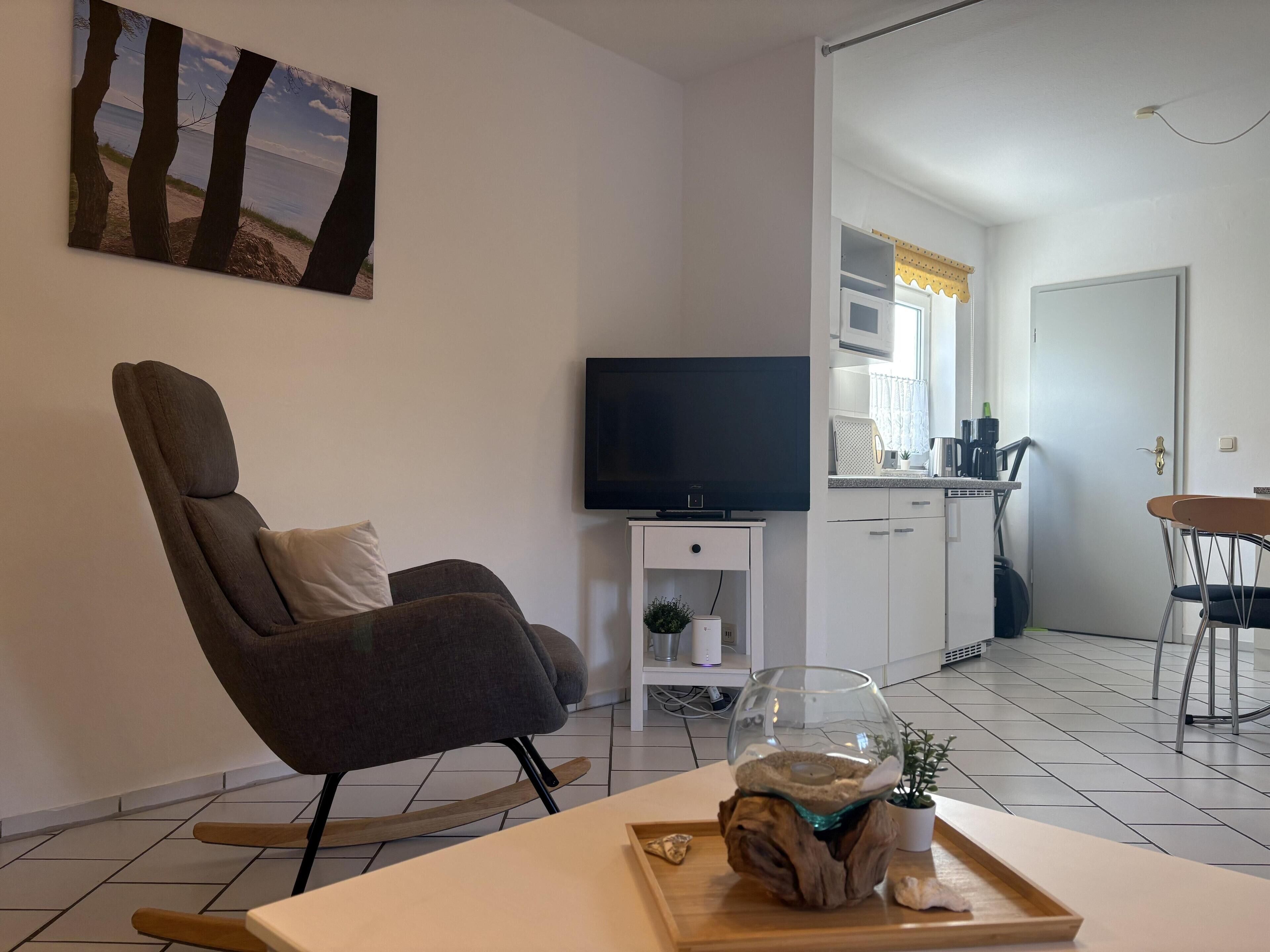 A modern living room with a sofa, a flat-screen TV, a glass fishbowl on a wooden base, and a dining area with a table and chairs.