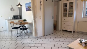 Una cucina moderna con zona pranzo, pavimento in piastrelle bianche e un armadietto bianco con ante in vetro.