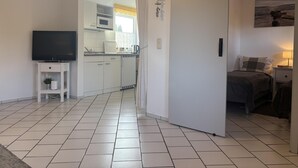 Una cucina moderna con mobili bianchi, un forno a microonde e un lavello. A sinistra, una televisione su un piccolo supporto.