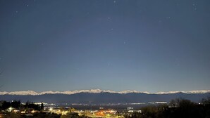 Une vue nocturne d’une ville, avec des montagnes enneigées en arrière-plan et une zone illuminée au premier plan.