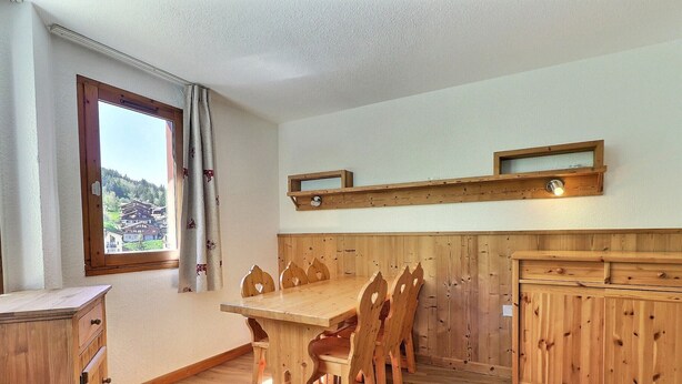 Une table à manger en bois avec des chaises, un buffet en bois et une fenêtre donnant sur des maisons.