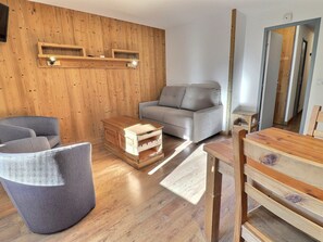 Una habitación con paneles de madera, un sofá, una pequeña mesa de madera y un sillón gris.