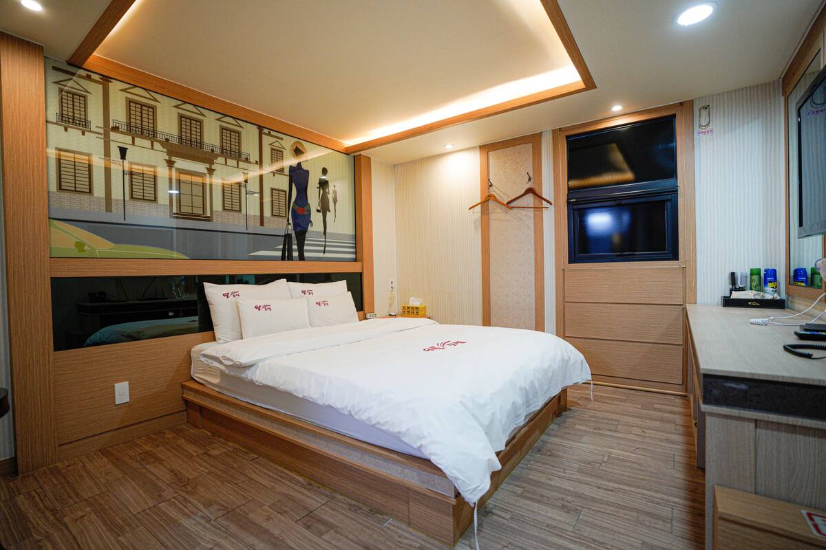 A modern hotel room with a large bed, built-in wardrobe, and a desk with a mirror.