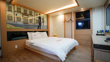A modern hotel room with a large bed, built-in wardrobe, and a desk with a mirror.