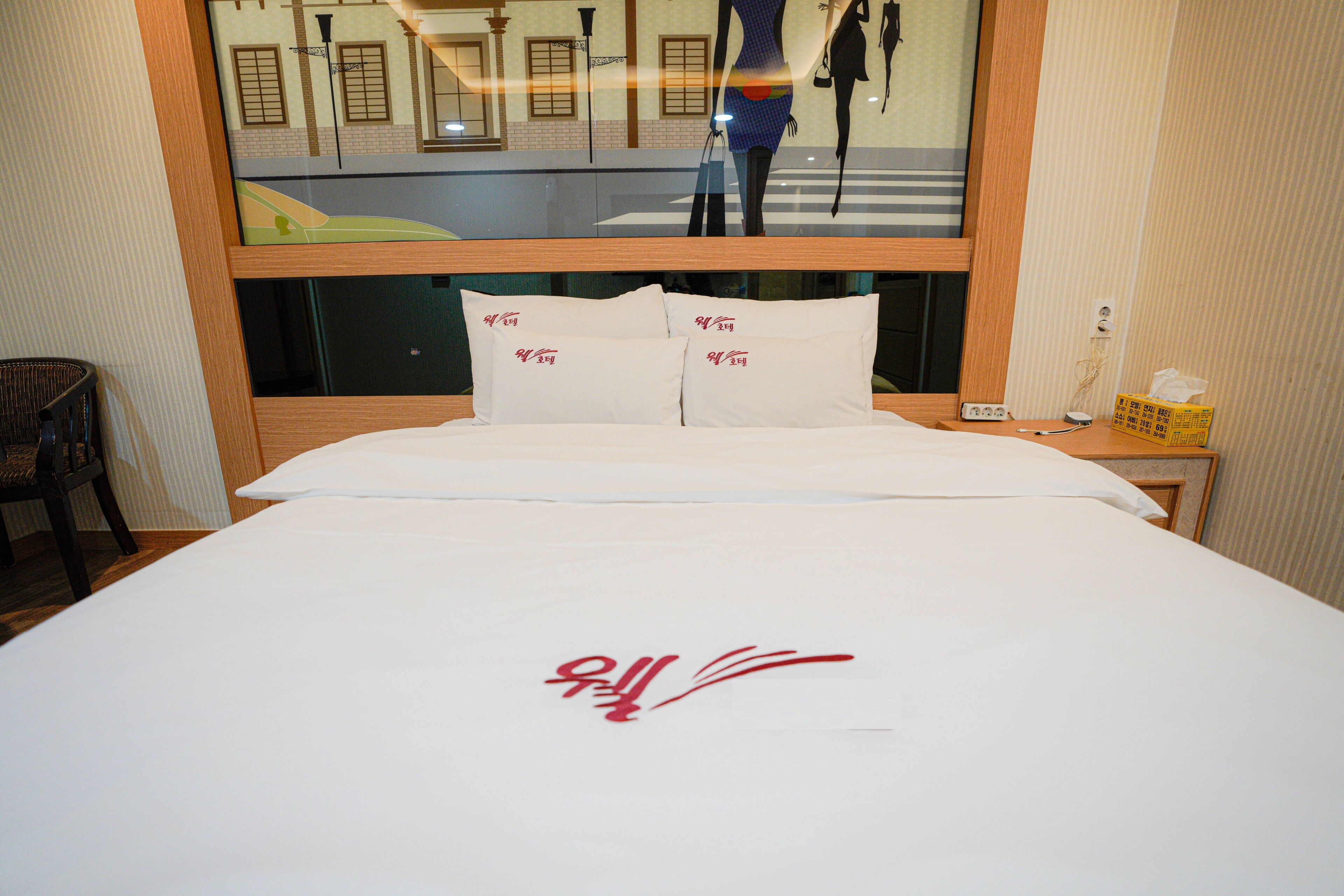 A hotel room with a large bed, a wooden headboard, and a window with a view of a street and buildings.