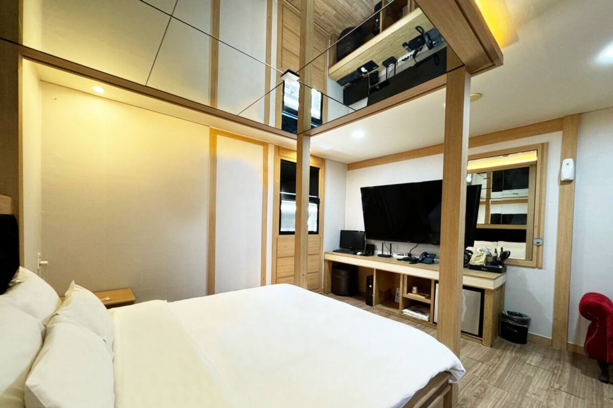 A bedroom with a large bed, a desk with a computer, and a TV.