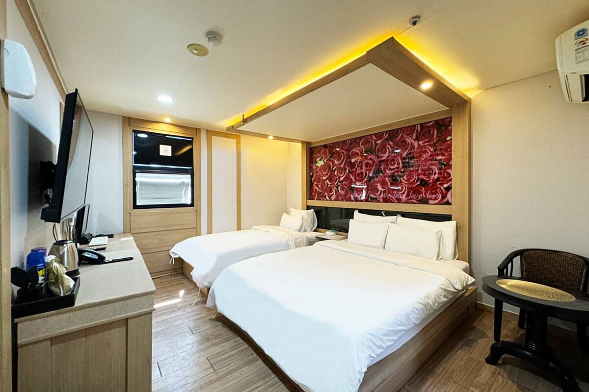 A hotel room with two beds, a desk with a computer, and a wall with a floral wallpaper.