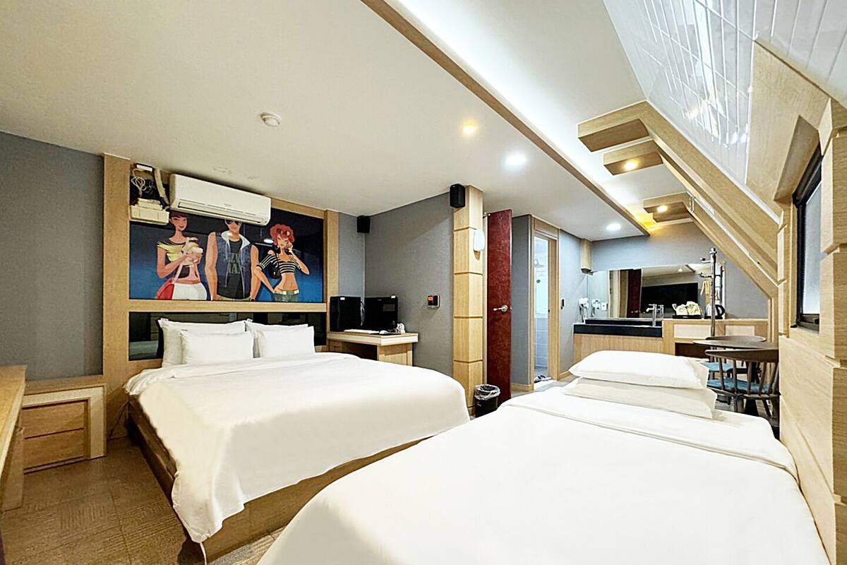 A hotel room with two beds, a desk, a TV, and a bathroom visible through an open door.