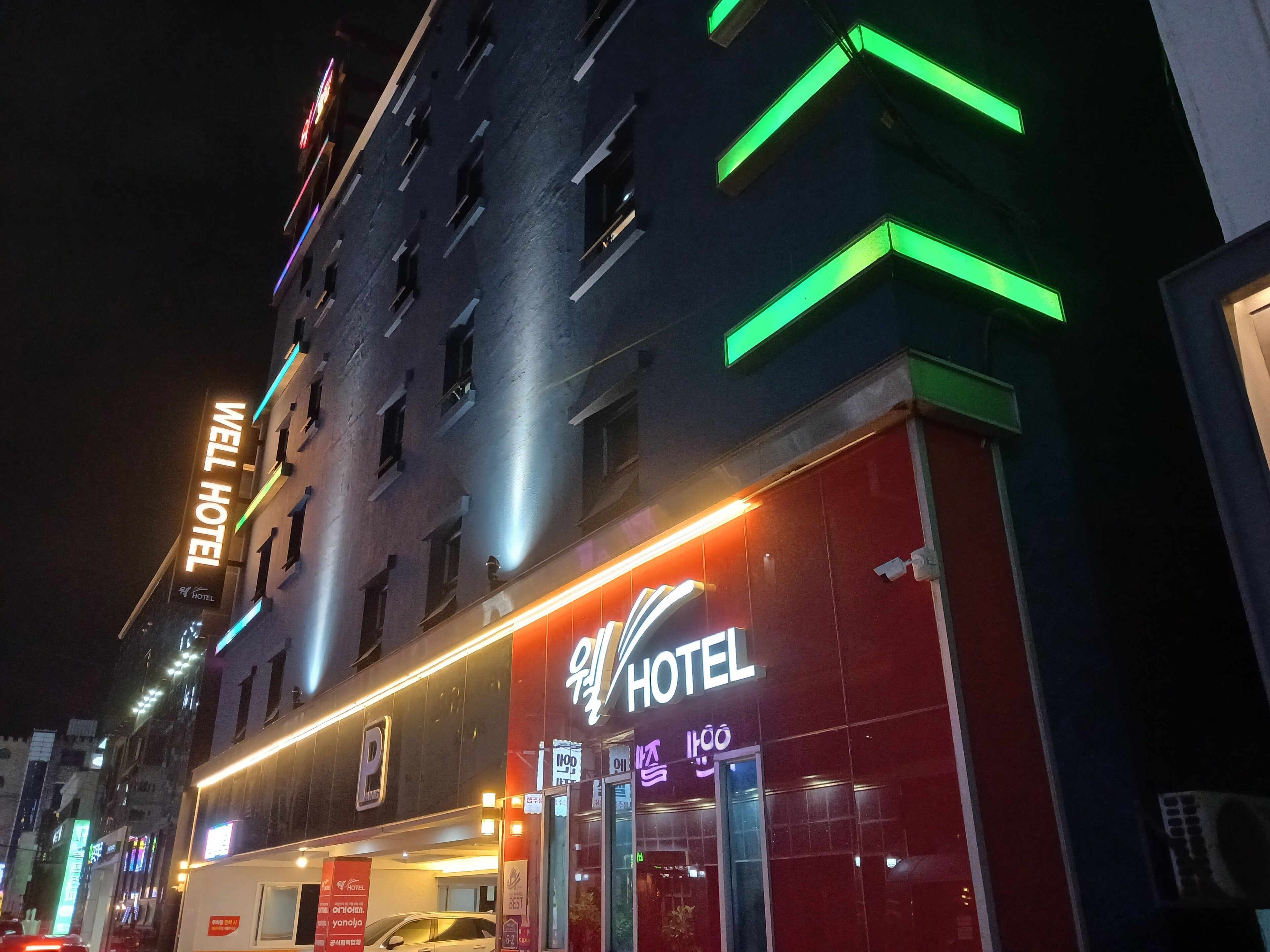A hotel with a prominent 'WELL HOTEL' sign, a parking area, and a red facade.