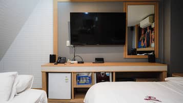 A hotel room with a bed, a desk with a television, a refrigerator, and a minibar.