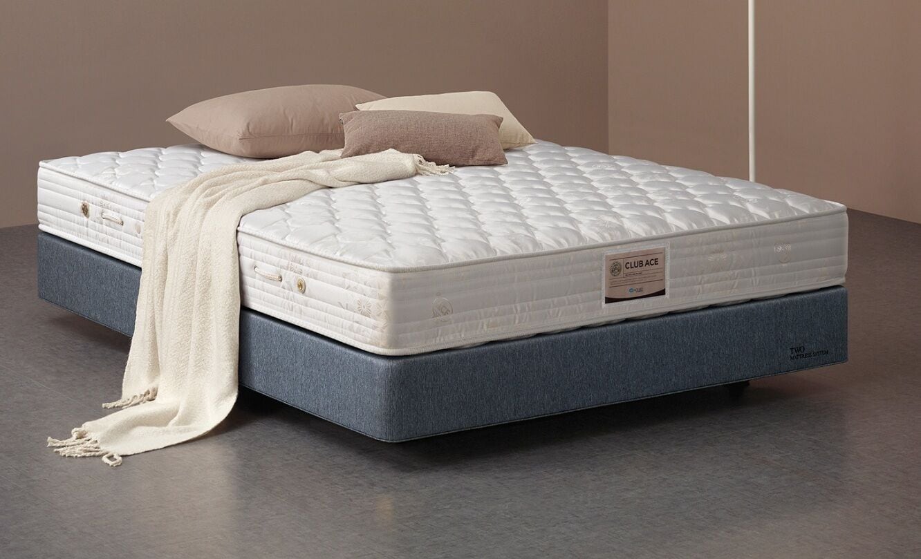 Una cama con colchón blanco, dos almohadas y una colcha blanca.
