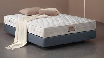 Una cama con colchón blanco, dos almohadas y una colcha blanca.