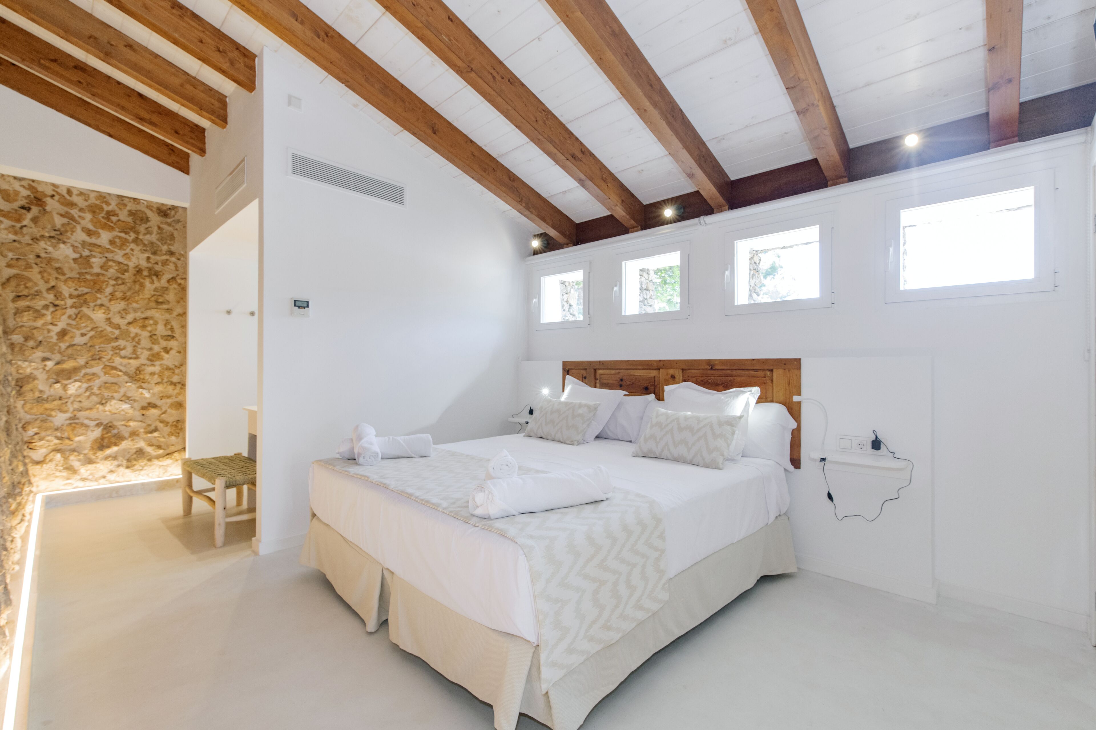 A bedroom with a large bed, wooden beams, stone wall, and a small window.