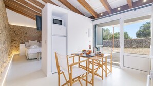 Ein modernes Zimmer mit Steinwand, einem Bett, einem weißen Kühlschrank, einem Esstisch mit Stühlen und einer großen Schiebeglasdoor, die zu einem Außenbereich führt.