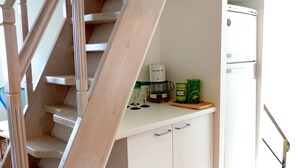 Ett kök med en trätrappa, vita skåp och ett litet kylskåp.
