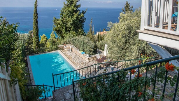En pool med en stenbelagd poolkant, omgiven av grönska och med utsikt över havet.