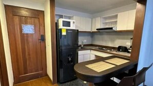 A compact kitchen with a refrigerator, microwave, and a small dining table with chairs. - Acogedor Apartasuite Cerca al Parque de la 93 (Bogotá)
