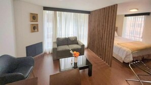 A modern hotel room with a sofa, a small table with a vase, a bed, and a window with curtains. - Acogedor Apartasuite Cerca al Parque de la 93 (Bogotá)