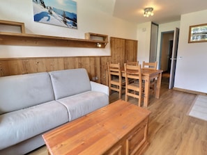 A living area with a sofa, wooden dining table, chairs, and a wooden cabinet.