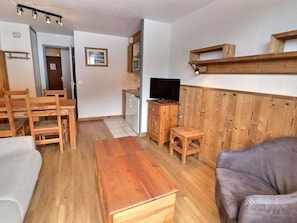 Un espace de vie compact comprenant une table à manger en bois, un canapé, un téléviseur et un coin cuisine.