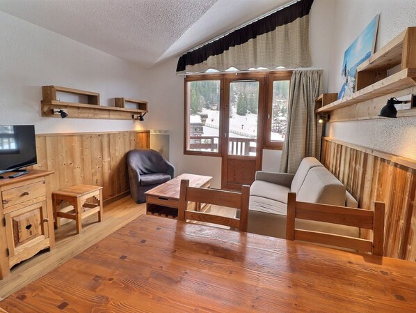 A cozy room with wooden furniture, a television, and a window with a view of a snowy landscape.