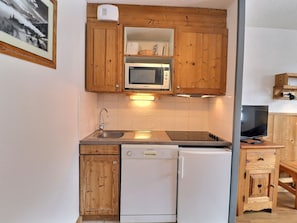 Une cuisine de taille réduite, dotée de meubles en bois, d’un four à micro-ondes, d’un lave-vaisselle et d’un téléviseur.