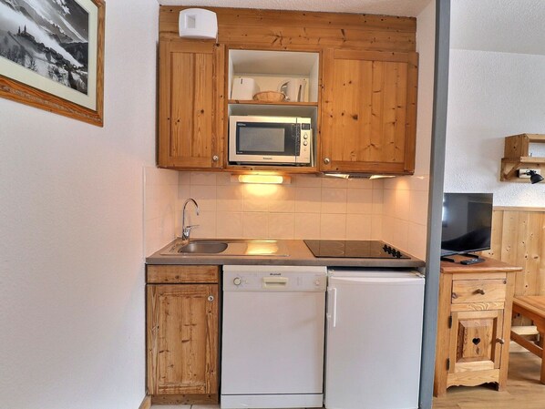 A compact kitchen with wooden cabinets, a microwave, a dishwasher, and a television.