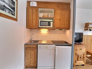 A compact kitchen with wooden cabinets, a microwave, a dishwasher, and a television.
