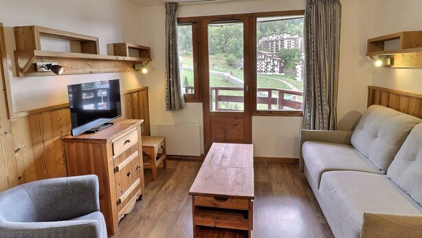 Ein gemütliches Zimmer mit einer Holz-TV-Konsole, einem Sofa, einem Holztisch und einem Fenster mit Blick auf Gebäude und Grünflächen.
