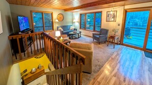 A spacious living area with a wooden ceiling, large windows, a television, and a sofa. - Gleason Lakefront House: Fire Pit, Kayak & Views! (Gleason)