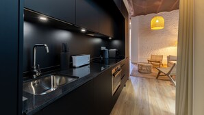 A modern kitchen with dark cabinetry, stainless steel appliances, and a wooden dining area with a woven chair and a lamp. - Triana Acacias by Valcambre  (Seville)