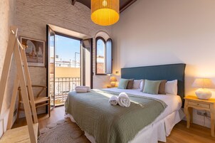 Un dormitorio con una cama grande, una escalera de madera, un balcón con vistas y una lámpara colgante.
