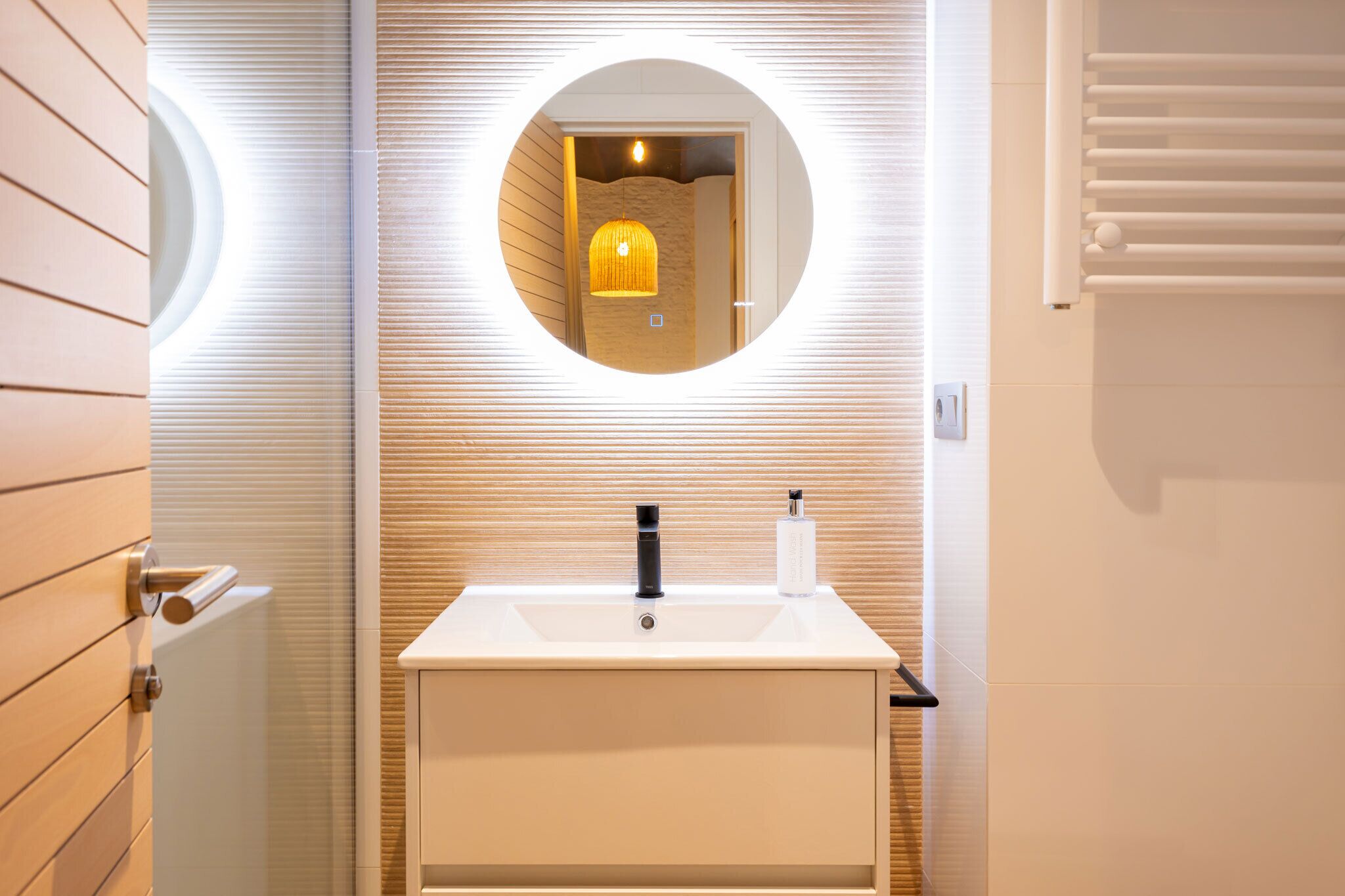 A bathroom with a white sink, a round mirror, and a towel rack.