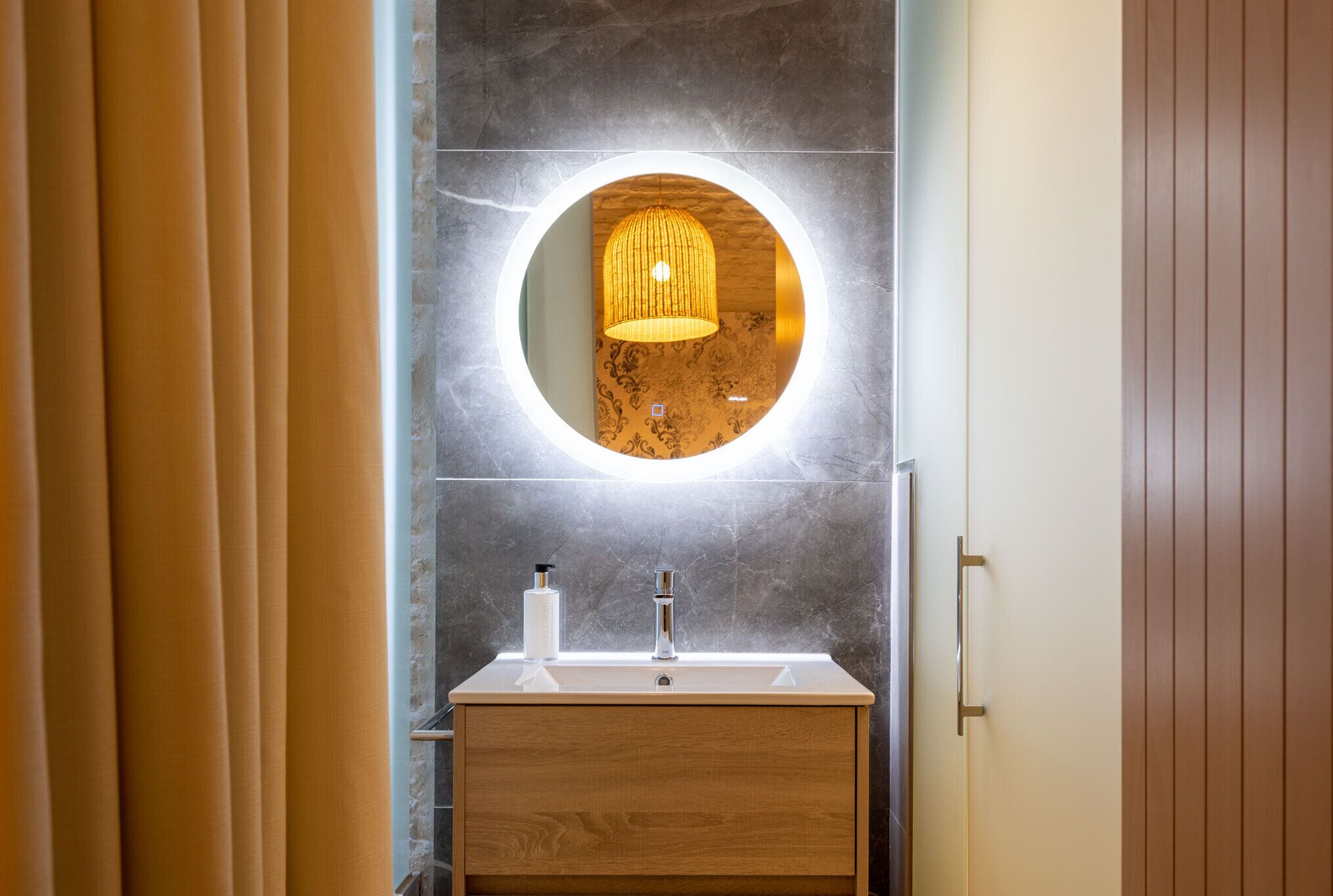 A bathroom with a wooden vanity, a round mirror, and a pendant light.