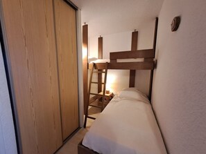 Ein kleines, kompaktes Zimmer mit einem Etagenbett, einem Holzschrank und einer Leiter.