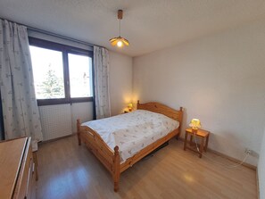 A bedroom with a wooden bed, a window with curtains, a bedside lamp, and a radiator.