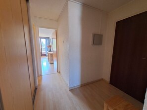 A hallway leading to a room with a dark door, a light-colored wall, and a small window.