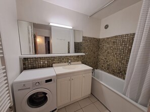 Ein kleines Badezimmer mit Waschmaschine, Waschbecken und Badewanne.