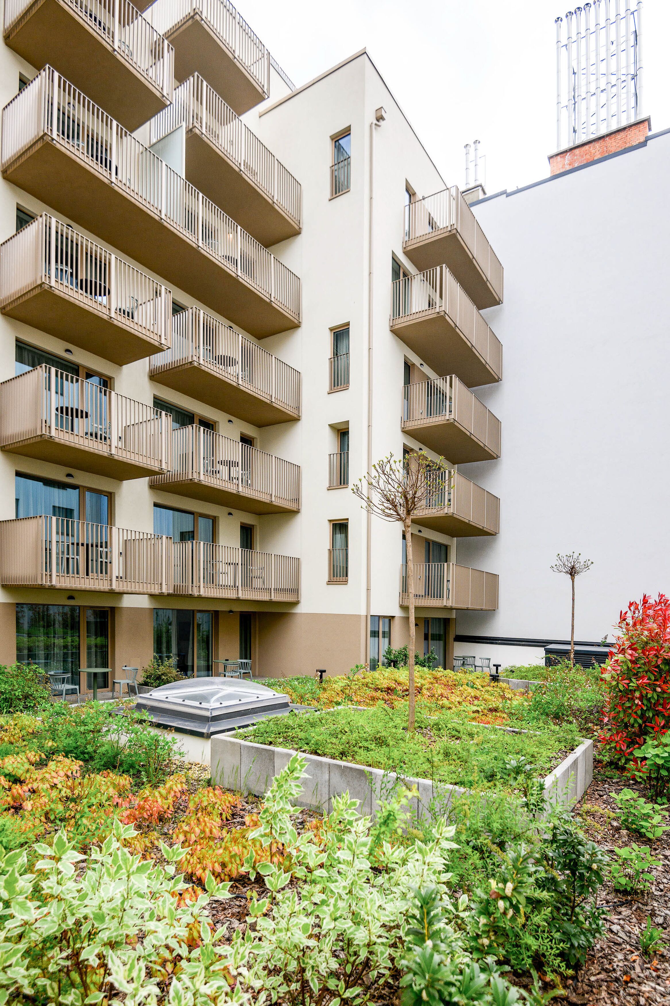 Un edificio de varios pisos con balcones y un jardín en la azotea.