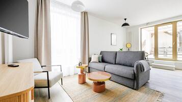 A modern living room with a grey sofa, a round coffee table, and a TV on a wooden stand.