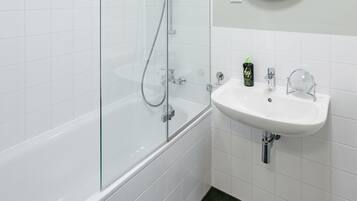 Un bagno moderno con doccia vetrata, lavandino bianco con specchio rotondo e piastrelle verde scuro al pavimento.