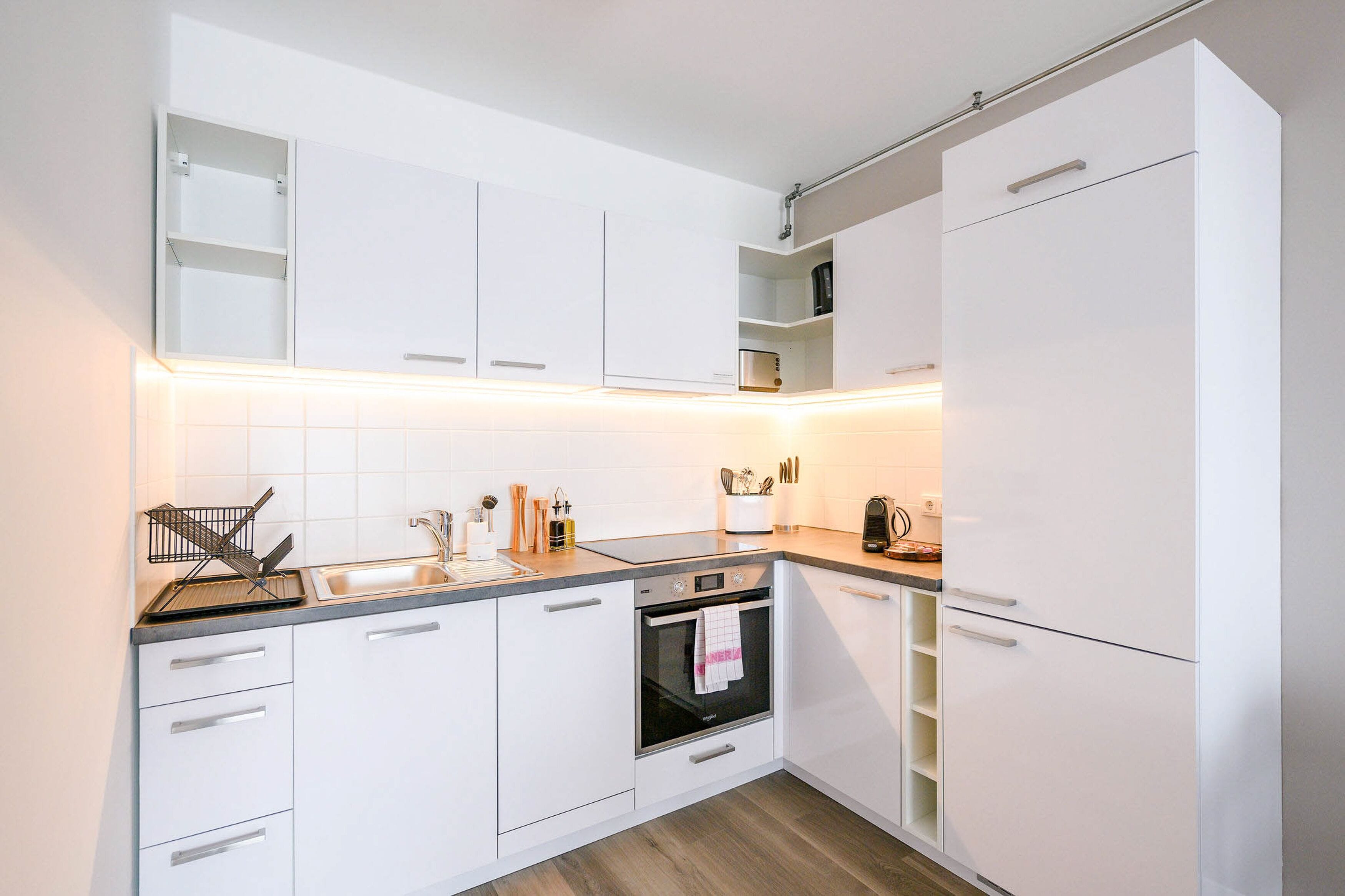 A modern kitchen with white cabinetry, a built-in oven, and a stainless steel sink.